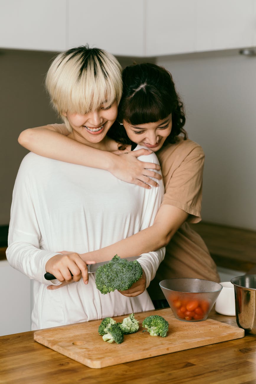 cheerful lesbian couple hugging and cooking dinner together